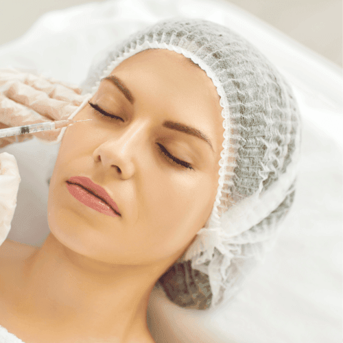 Woman receiving cosmetic injection in facial area, wearing a hair cover and lying down during the procedure.